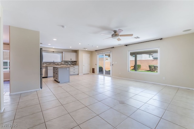 unfurnished living room with visible vents, a ceiling fan, a sink, light tile patterned flooring, and baseboards