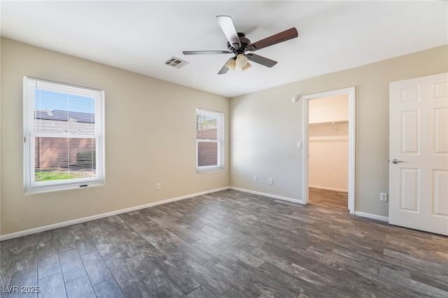 unfurnished bedroom with visible vents, dark wood-style flooring, baseboards, ceiling fan, and a spacious closet