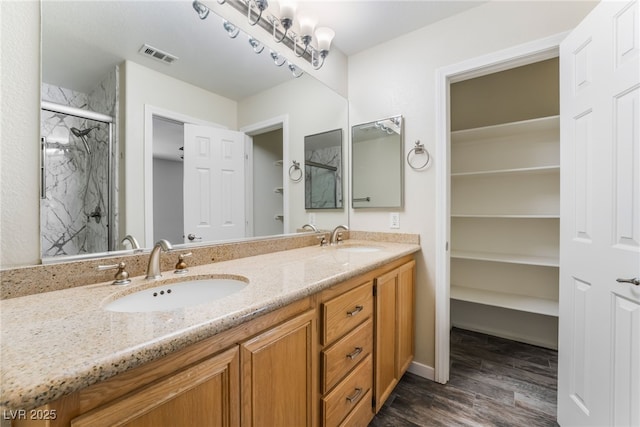 full bath with wood finished floors, visible vents, a marble finish shower, and a sink