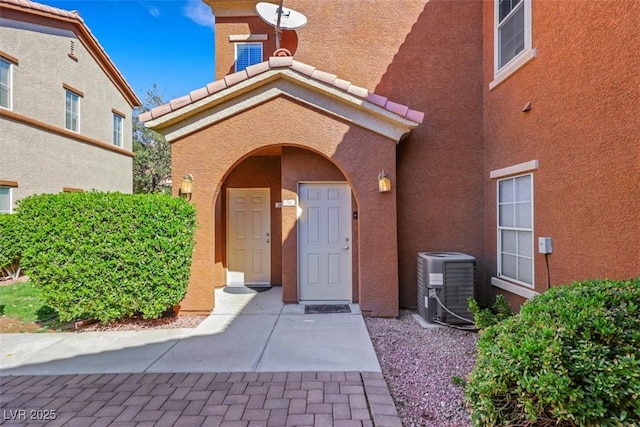 doorway to property featuring stucco siding, central AC unit, and a tiled roof