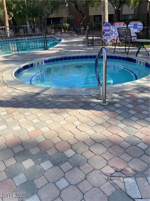 community pool with a patio area, fence, and a hot tub