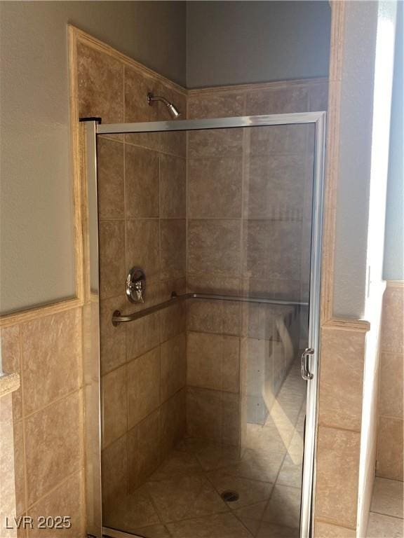 full bath with a wainscoted wall, tile walls, and a stall shower