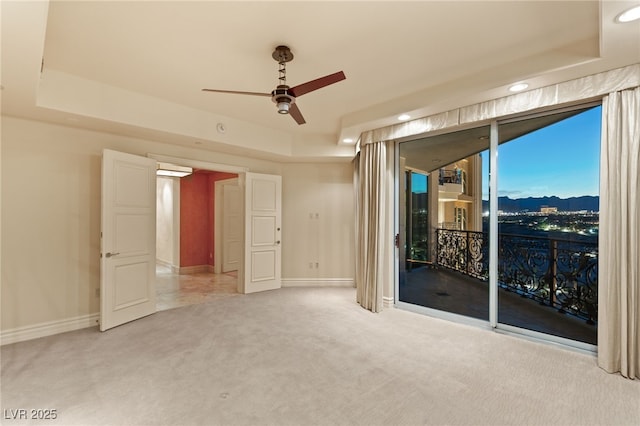 spare room featuring light colored carpet, a raised ceiling, baseboards, and ceiling fan