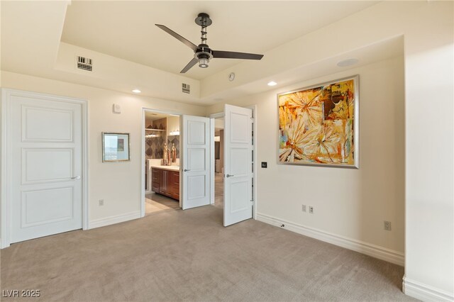 unfurnished bedroom with visible vents, light carpet, a tray ceiling, ensuite bath, and baseboards