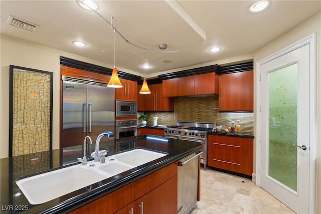 kitchen with dark countertops, visible vents, built in appliances, pendant lighting, and a sink