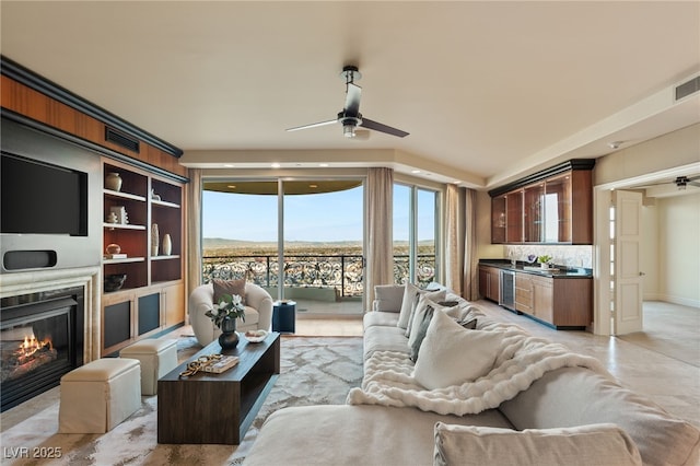 living room featuring a glass covered fireplace, beverage cooler, a ceiling fan, and visible vents