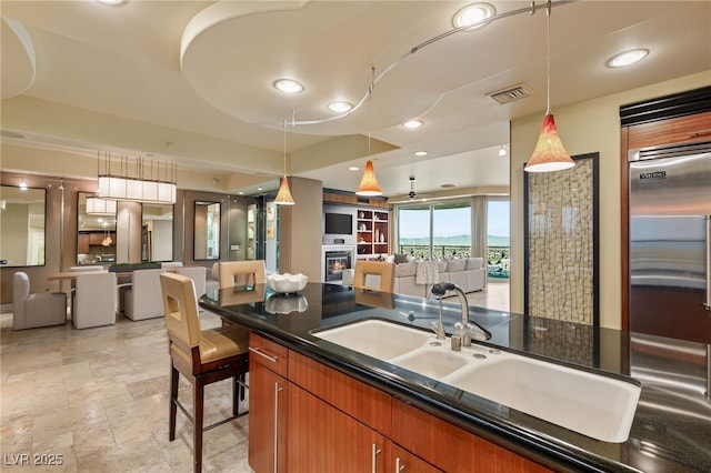 kitchen featuring visible vents, open floor plan, a lit fireplace, brown cabinets, and a sink