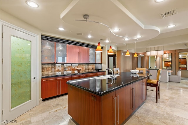 kitchen with dark countertops, visible vents, a kitchen island with sink, and a sink