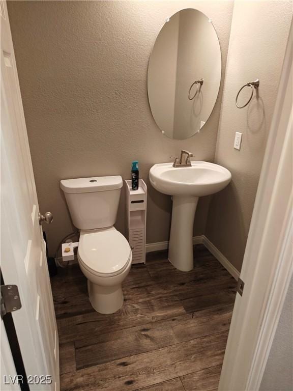 bathroom featuring wood finished floors, baseboards, a sink, toilet, and a textured wall