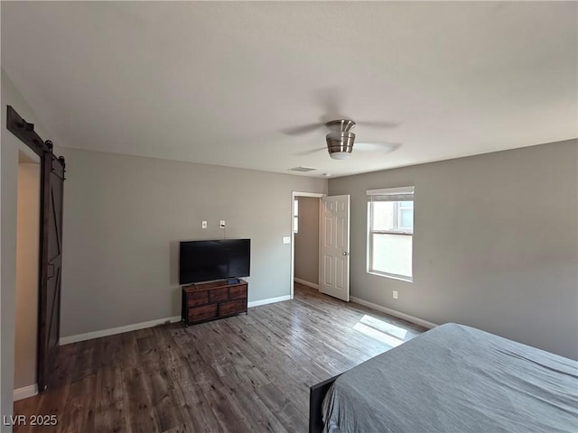 unfurnished bedroom with a ceiling fan, dark wood-style floors, baseboards, visible vents, and a barn door