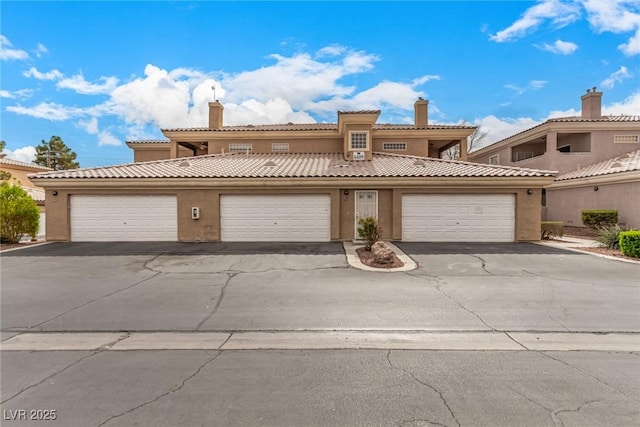 view of front of house featuring stucco siding, an attached garage, a chimney, and driveway