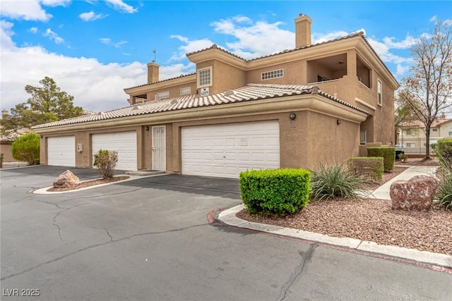 view of front of property with aphalt driveway, an attached garage, a chimney, and stucco siding