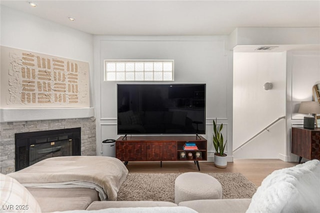 living area with visible vents, a stone fireplace, and wood finished floors