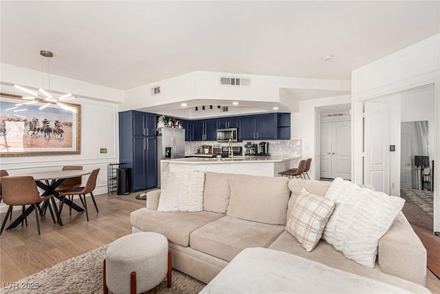 living area featuring light wood-style floors, visible vents, and a chandelier