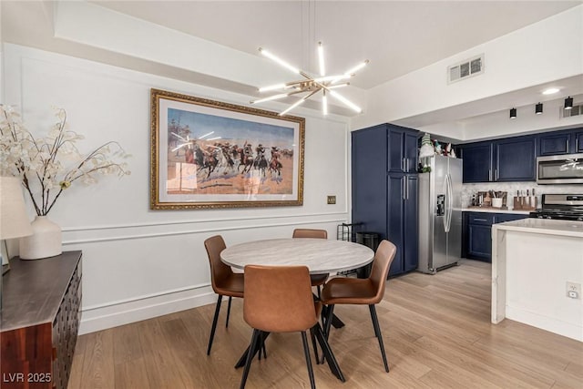 dining space featuring an inviting chandelier, a raised ceiling, light wood-style floors, and visible vents