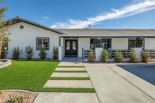 view of front of house featuring a front lawn, a porch, stucco siding, french doors, and a chimney