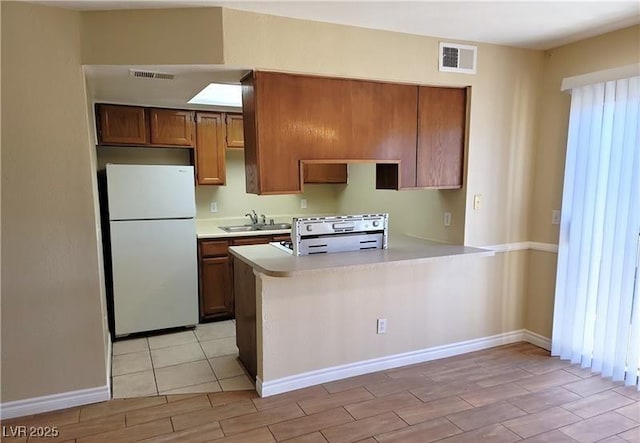 kitchen featuring brown cabinetry, visible vents, light countertops, and freestanding refrigerator