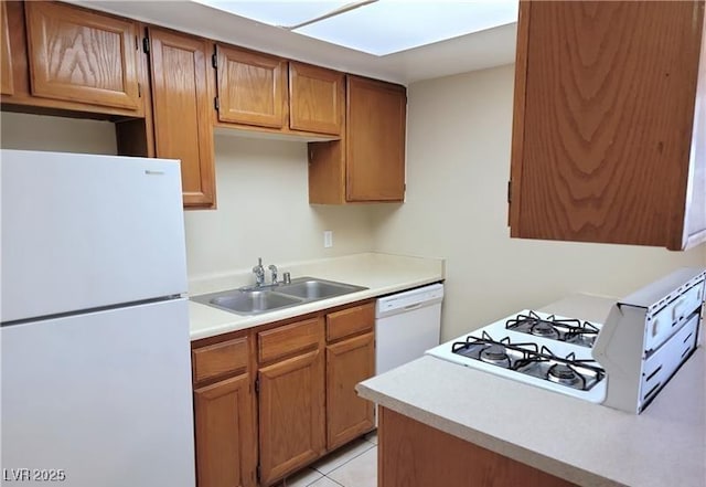 kitchen featuring light countertops, a skylight, light tile patterned flooring, white appliances, and a sink