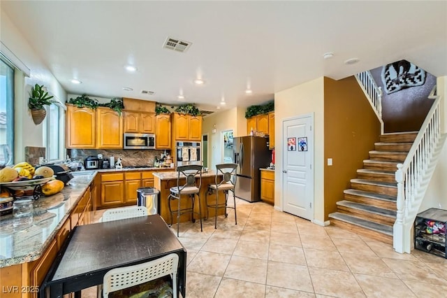 kitchen with a kitchen island, tasteful backsplash, appliances with stainless steel finishes, light tile patterned flooring, and light stone countertops