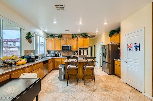 kitchen featuring visible vents, decorative backsplash, appliances with stainless steel finishes, a kitchen breakfast bar, and a sink