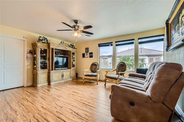 living area featuring baseboards, light wood-style floors, and a ceiling fan