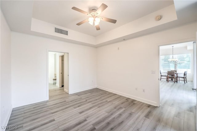 unfurnished room with light wood finished floors, visible vents, baseboards, ceiling fan with notable chandelier, and a raised ceiling