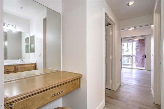 corridor with light wood-style flooring, recessed lighting, baseboards, and a sink