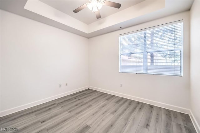 unfurnished room with a ceiling fan, a tray ceiling, baseboards, and light wood-type flooring