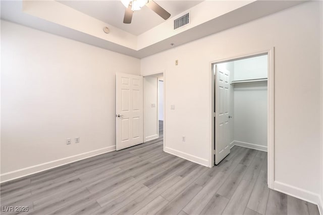 unfurnished bedroom with visible vents, baseboards, light wood-type flooring, and a tray ceiling