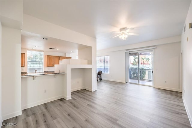 unfurnished living room with baseboards, plenty of natural light, a ceiling fan, and light wood finished floors