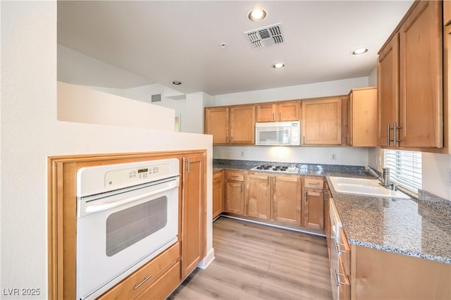 kitchen featuring visible vents, a sink, recessed lighting, white appliances, and light wood finished floors