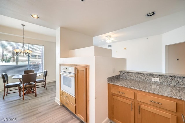 kitchen with light stone countertops, recessed lighting, oven, light wood-style floors, and pendant lighting