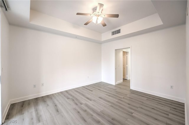 spare room with visible vents, a raised ceiling, wood finished floors, and a ceiling fan