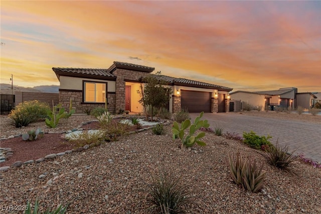 view of front of property with a tile roof, stucco siding, a garage, stone siding, and driveway