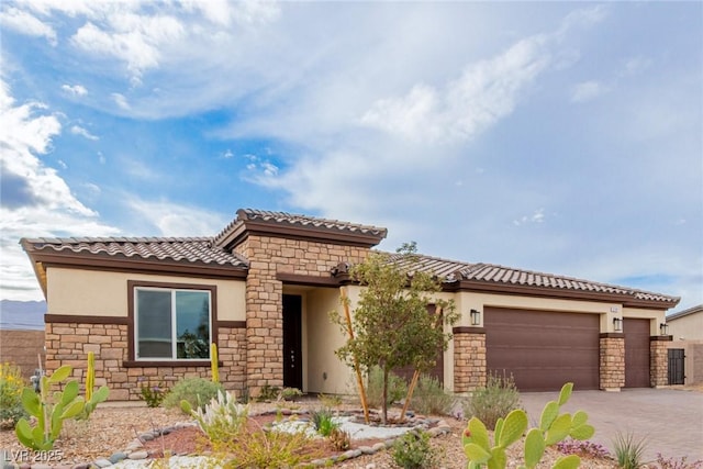 mediterranean / spanish house with stucco siding, driveway, a tile roof, stone siding, and a garage