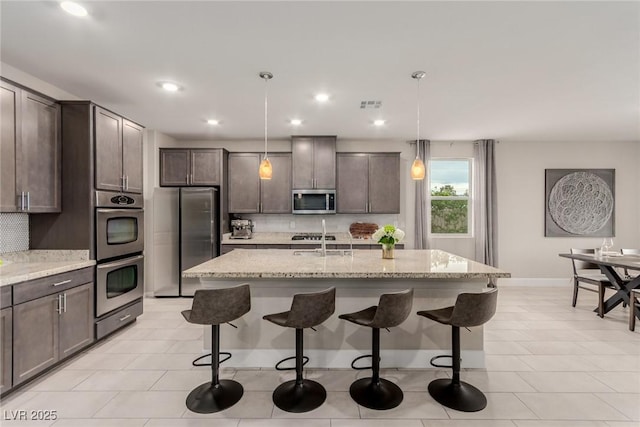 kitchen with a breakfast bar, light stone counters, stainless steel appliances, dark brown cabinetry, and decorative backsplash