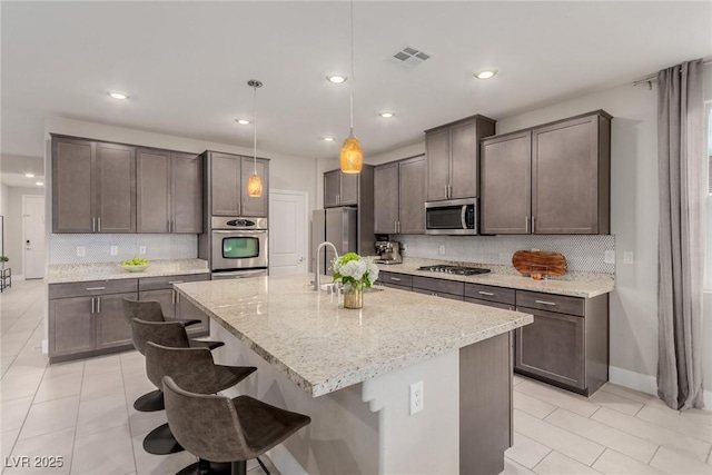 kitchen featuring visible vents, dark brown cabinets, light stone counters, appliances with stainless steel finishes, and a kitchen breakfast bar