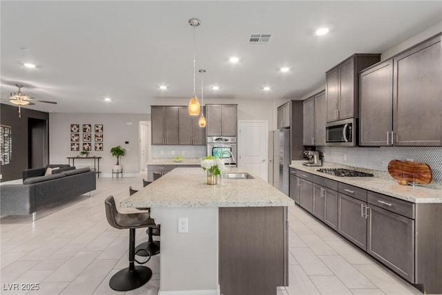 kitchen featuring a breakfast bar area, visible vents, appliances with stainless steel finishes, open floor plan, and backsplash