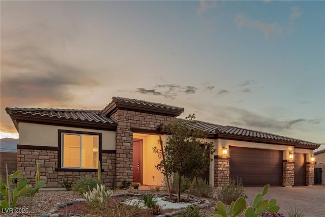 view of front facade with decorative driveway, a garage, stone siding, and stucco siding