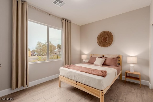 bedroom featuring light wood-style floors, visible vents, and baseboards