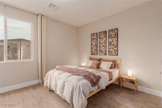 bedroom with light wood-style floors, visible vents, and baseboards