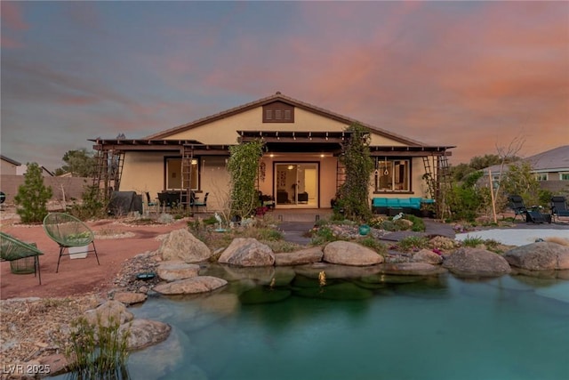 back of house at dusk with a garden pond, a patio, and stucco siding