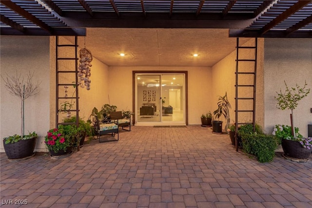 entrance to property with a patio area, stucco siding, and a pergola