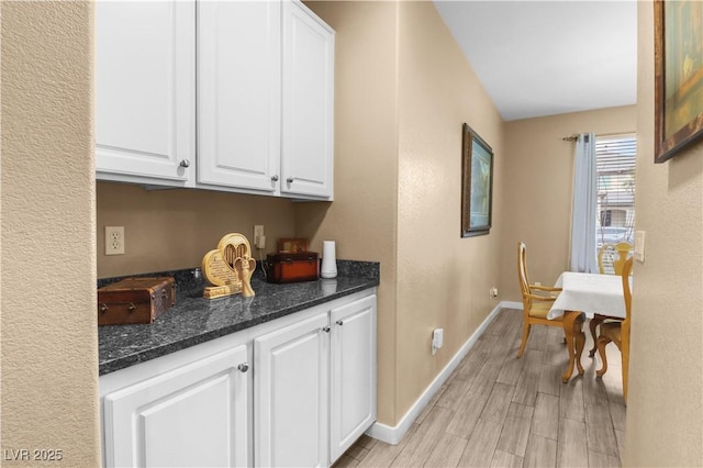 kitchen with dark stone countertops, baseboards, wood tiled floor, and white cabinetry