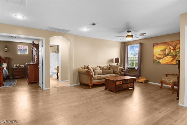 living room featuring light wood finished floors, visible vents, baseboards, arched walkways, and a ceiling fan