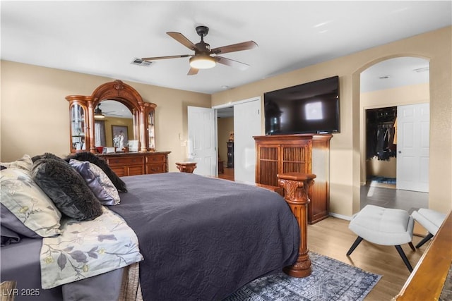 bedroom with ceiling fan, visible vents, arched walkways, and wood finished floors