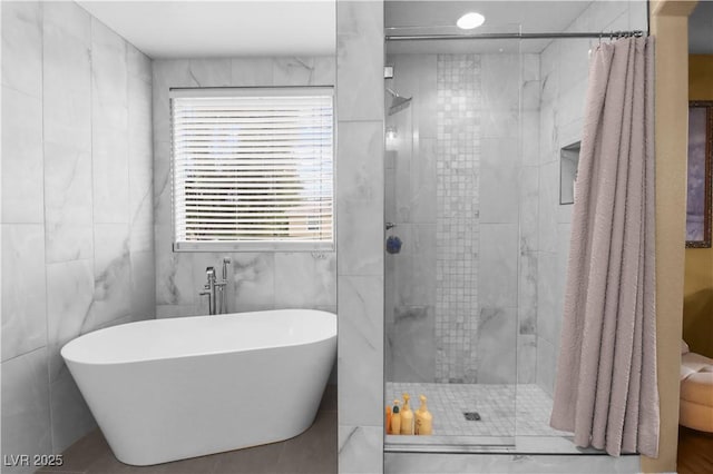 bathroom with a soaking tub, a stall shower, and tile walls