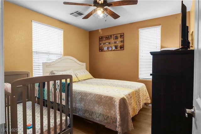 bedroom featuring visible vents, multiple windows, wood finished floors, and a ceiling fan