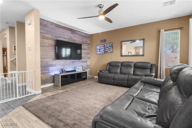 living area featuring wooden walls, visible vents, an accent wall, arched walkways, and a ceiling fan