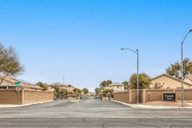 view of road featuring sidewalks, curbs, street lighting, and a gate